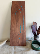 Load image into Gallery viewer, Full-length black walnut serving board standing upright, showing its natural edge and turquoise inlay pattern