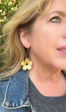 Load image into Gallery viewer, Close-up of a woman wearing gold flower-shaped earrings with a blurred outdoor background.