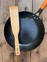 Load image into Gallery viewer, Camper maple wood cooking paddle with a broad blade and long handle, resting across a black skillet on rustic wood.
