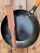 Load image into Gallery viewer, Camper walnut wood cooking paddle with a broad blade and long handle, resting across a black skillet on rustic wood.
