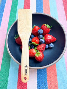handcrafted wooden kitchen untensil in maple wood pictured with a bowl of strawberries and blue berries
