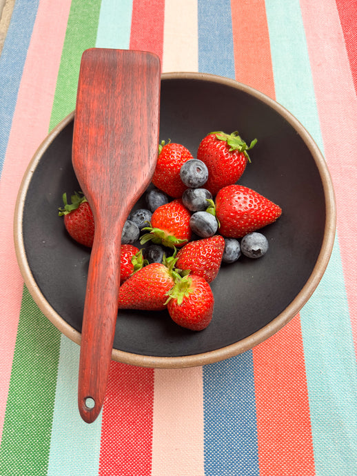 handcrafted wooden kitchen untensil in padauk wood pictured with a bowl of strawberries and blue berries