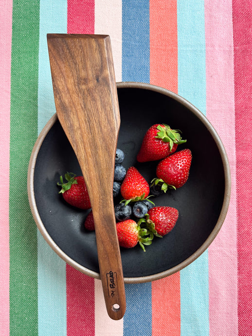 walnut handcrafted spatula pictured with a bowl of strawberries and blueberries
