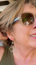 Load image into Gallery viewer, A close-up lifestyle shot of a woman wearing a silver wire heart-shaped hoop earring, clear-framed sunglasses, and a green top.

